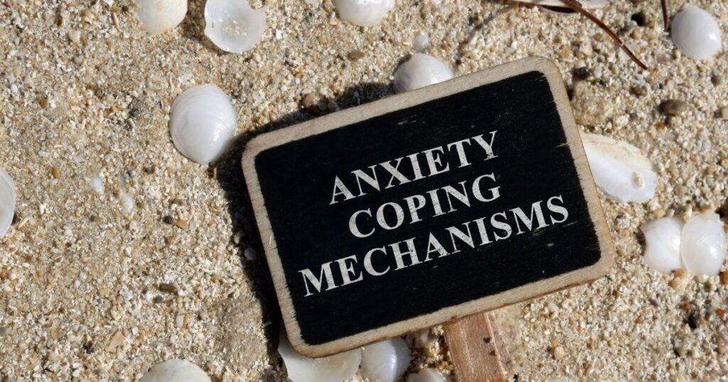 black sign on sand with shells, white text: anxiety coping mechanisms
