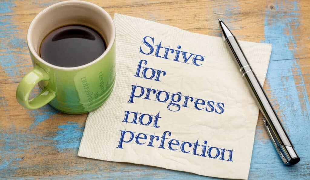 flat lay, green mug, pen, and napkin with words "Strive for progress not perfection"