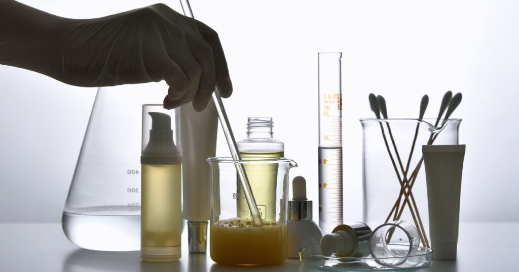 scientist formulating skincare products, graduated cylinder, beaker with chemicals, personal care bottles, cotton swabs